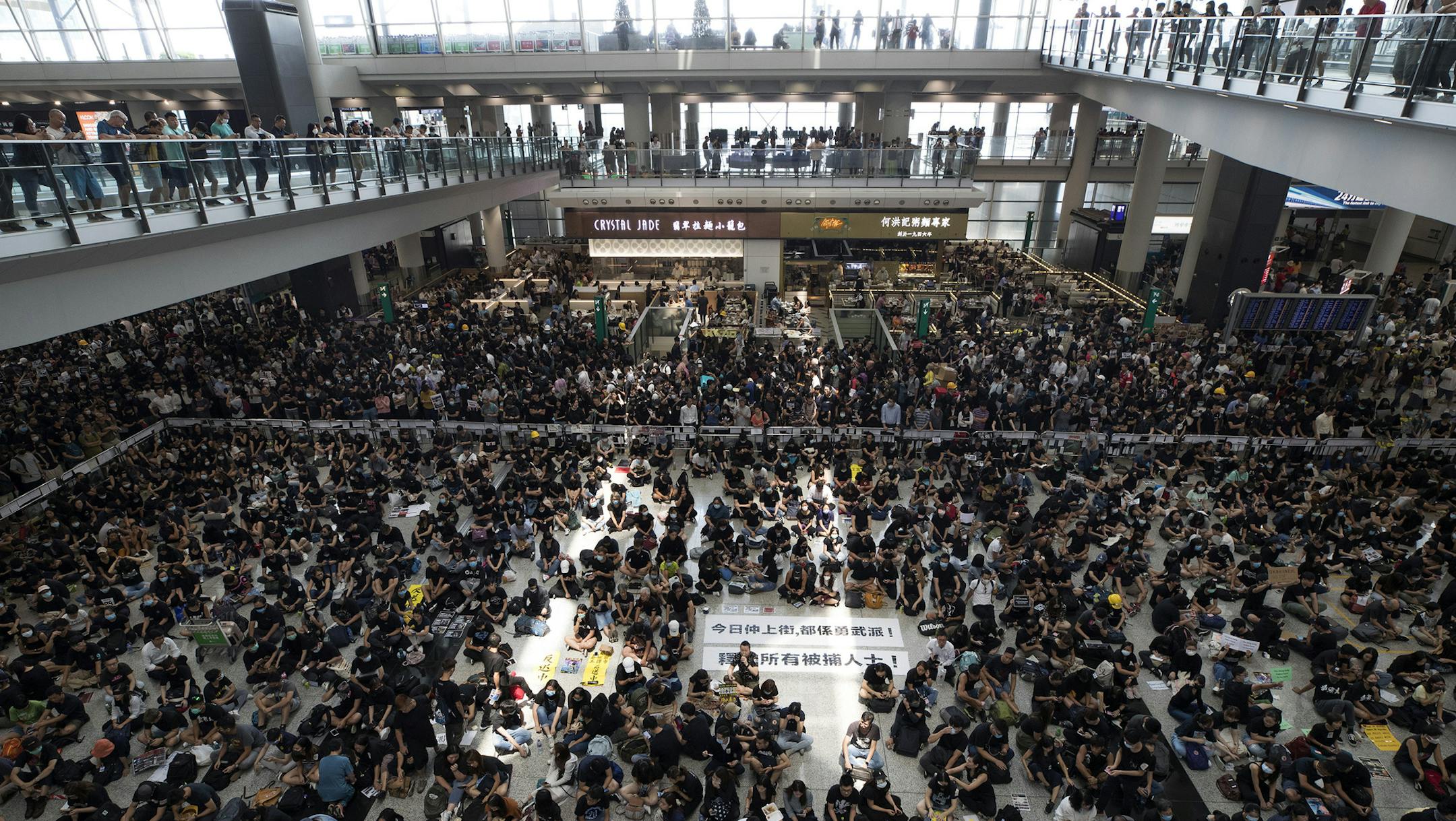 Protesters surround banners that read: "Those charge to the street on today is brave!," center top, and "Release all the detainees!" during a sit-in rally at the arrival hall of the Hong Kong International airport, Monday, Aug. 12, 2019. Hong Kong police showed off water cannons Monday as pro-democracy street protests stretched into their 10th week with no sign of either side backing down. (AP Photo/Vincent Thian)