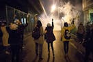 In this photograph taken Saturday, Jan. 11, 2020, protesters hold flowers as tear gas fired by police rises at a demonstration in front of Amir Kabir 