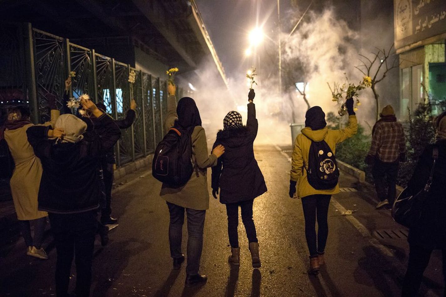 In this photograph taken Saturday, Jan. 11, 2020, protesters hold flowers as tear gas fired by police rises at a demonstration in front of Amir Kabir University in Tehran, Iran, to remember victims of a Ukrainian airplane shot down by an Iranian missile. On Monday, Jan. 13, 2020, online videos purported to show that Iranian security forces fired both live ammunition and tear gas to disperse demonstrators protesting against the Islamic Republic's initial denial that it shot down a Ukrainian jetli