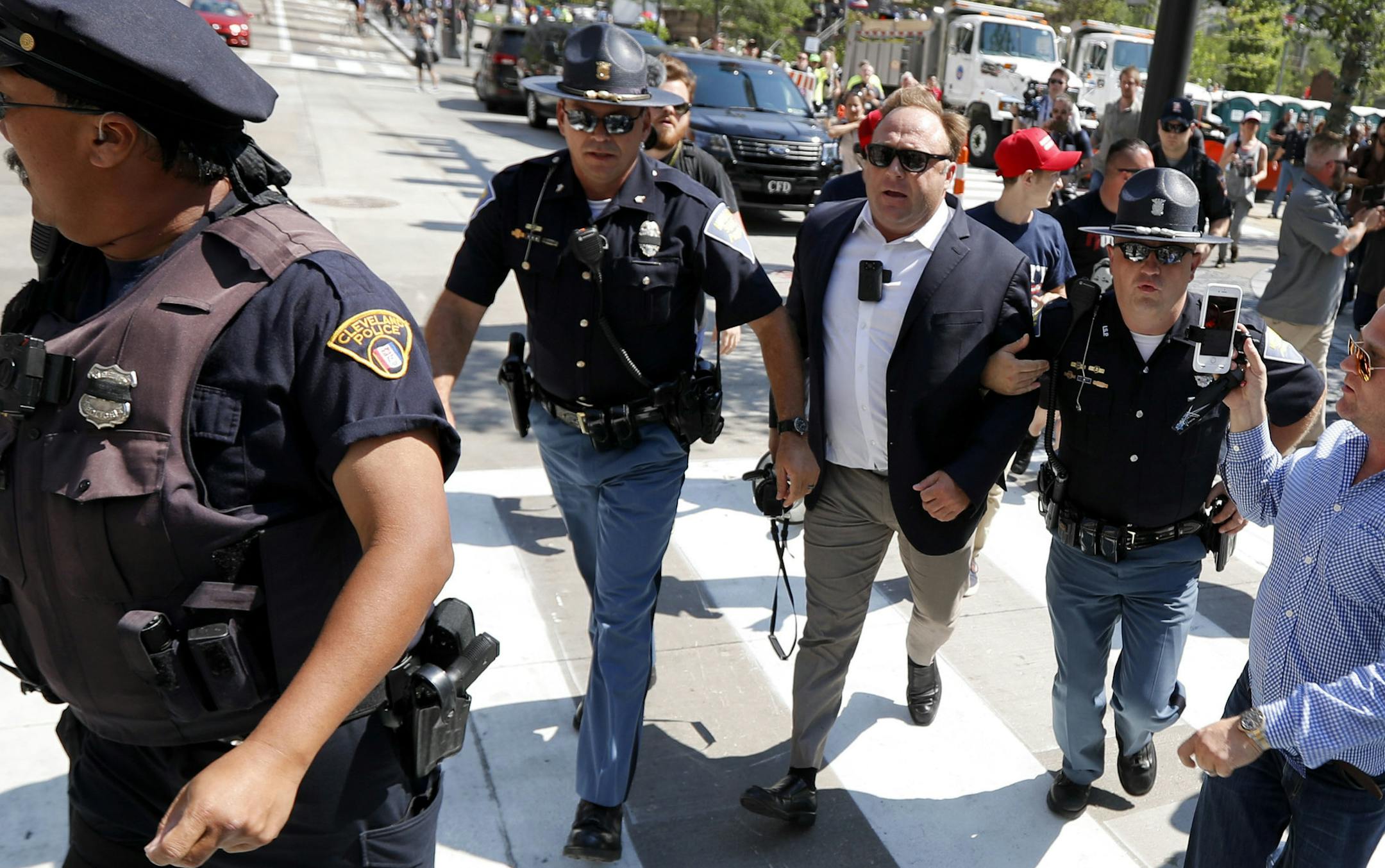 FILE - In this Tuesday, July 19, 2016 file photo, Alex Jones, center right, is escorted by police out of a crowd of protesters outside the Republican convention in Cleveland. Facebook says it has taken down four pages belonging to conspiracy theorist Alex Jones for violating its hate speech and bullying policies. The social media giant said in a statement Monday, Aug. 6, 2018 that it also blocked Jones' account for 30 days because he repeatedly posted content that broke its rules. (AP Photo/John