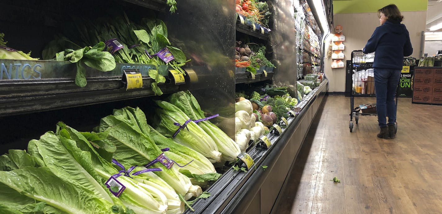 FILE - In this Nov. 20, 2018 file photo, romaine lettuce sits on the shelves as a shopper walks through the produce area of an Albertsons market in Simi Valley, Calif. After repeated food poisoning outbreaks linked to romaine lettuce, the produce industry is confronting the failure of its own safety measures in preventing contaminations. The latest outbreak underscores the challenge of eliminating risk for vegetables grown in open fields and eaten raw. It also highlights the role of nearby cattl