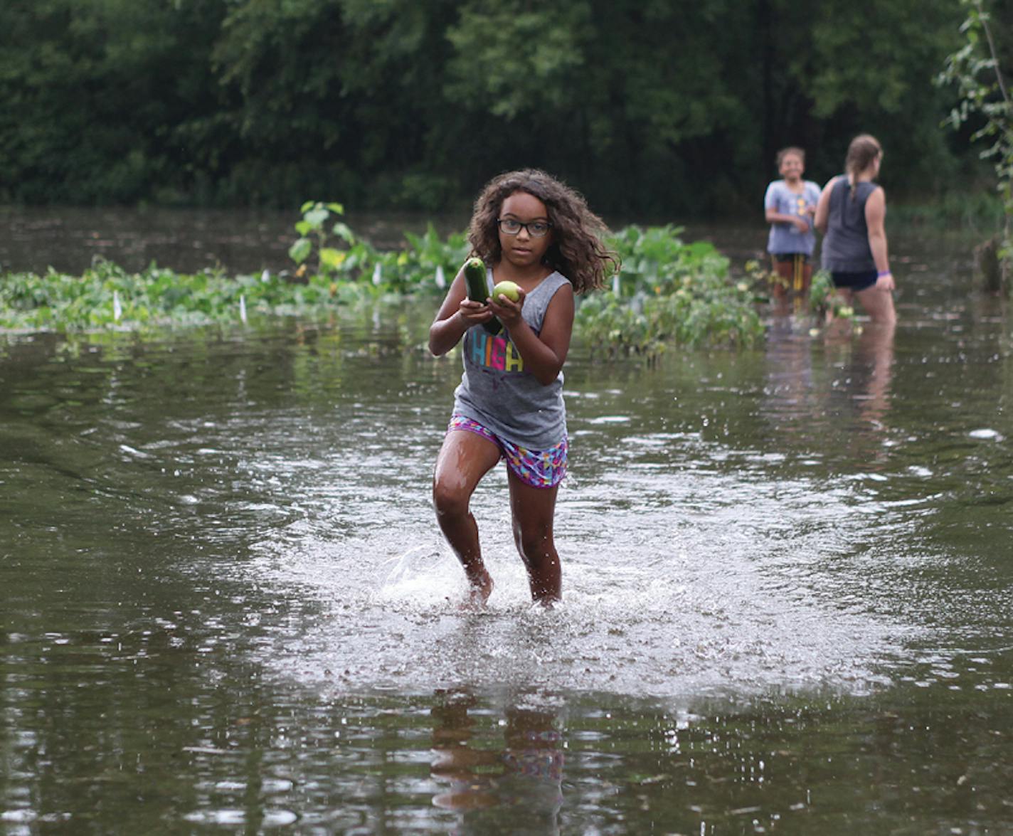 Brooklynn Harmon of Saukville, Wis., carries food from her grandmother's, Eileen Kudek, garden Monday, Aug. 27, 2018, in the town of Trenton, Wis. Another drenching storm has dumped more than 7 inches of rain on parts of Ozaukee and Washington counties. (Nicholas Dettmann/West Bend Daily News via AP)