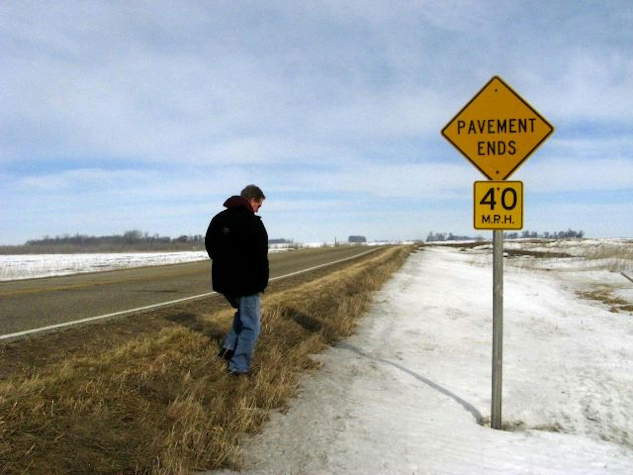 Freeborn County Commissioner Glen Mathiason stands near a small stretch of County Road 30 that workers reverted to gravel because it was too expensive to maintain pavement on marshy ground.
