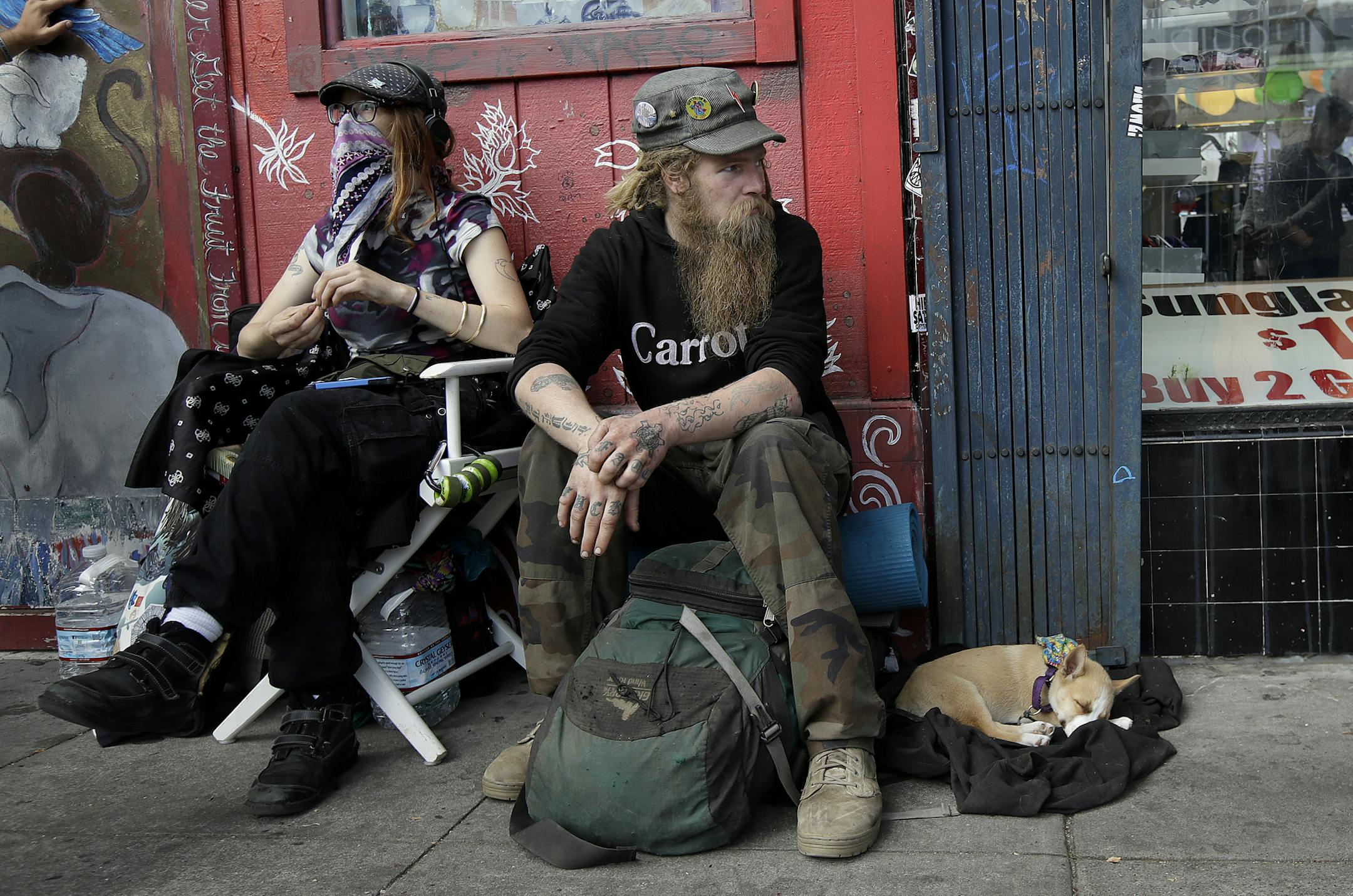 In this Oct. 1, 2018 photo, Stormy Nichole Day, left, sits on a sidewalk on Haight Street with Nord (last name not given) and his dog Hobo while interviewed about being homeless in San Francisco. A measure on San Francisco's Nov. 6 ballot would levy an extra tax on hundreds of the city's wealthiest companies to raise $300 million for homelessness and mental health services. It's the latest battle between big business and social services advocates who say that companies such as Amazon, Google and