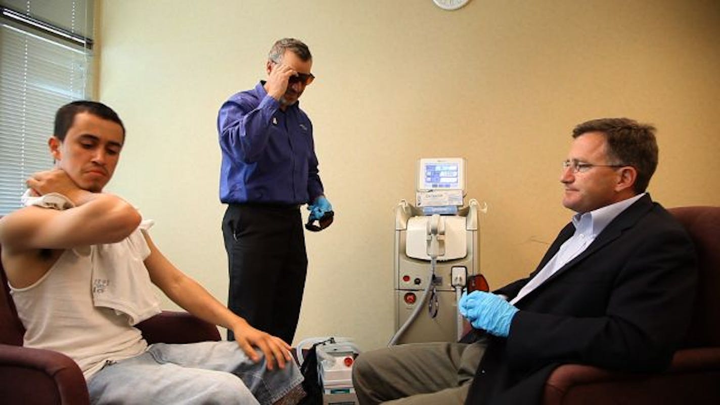 Albert Gomez, 19, looked at his arm after Dr. Joseph Campanelli, right, finished his work with the laser Monday afternoon at St. Paul's Neighborhood House. It typically takes between 6 and 12 sessions, with four to six weeks in between, to remove a tattoo. This was probably Gomez's last treatment.