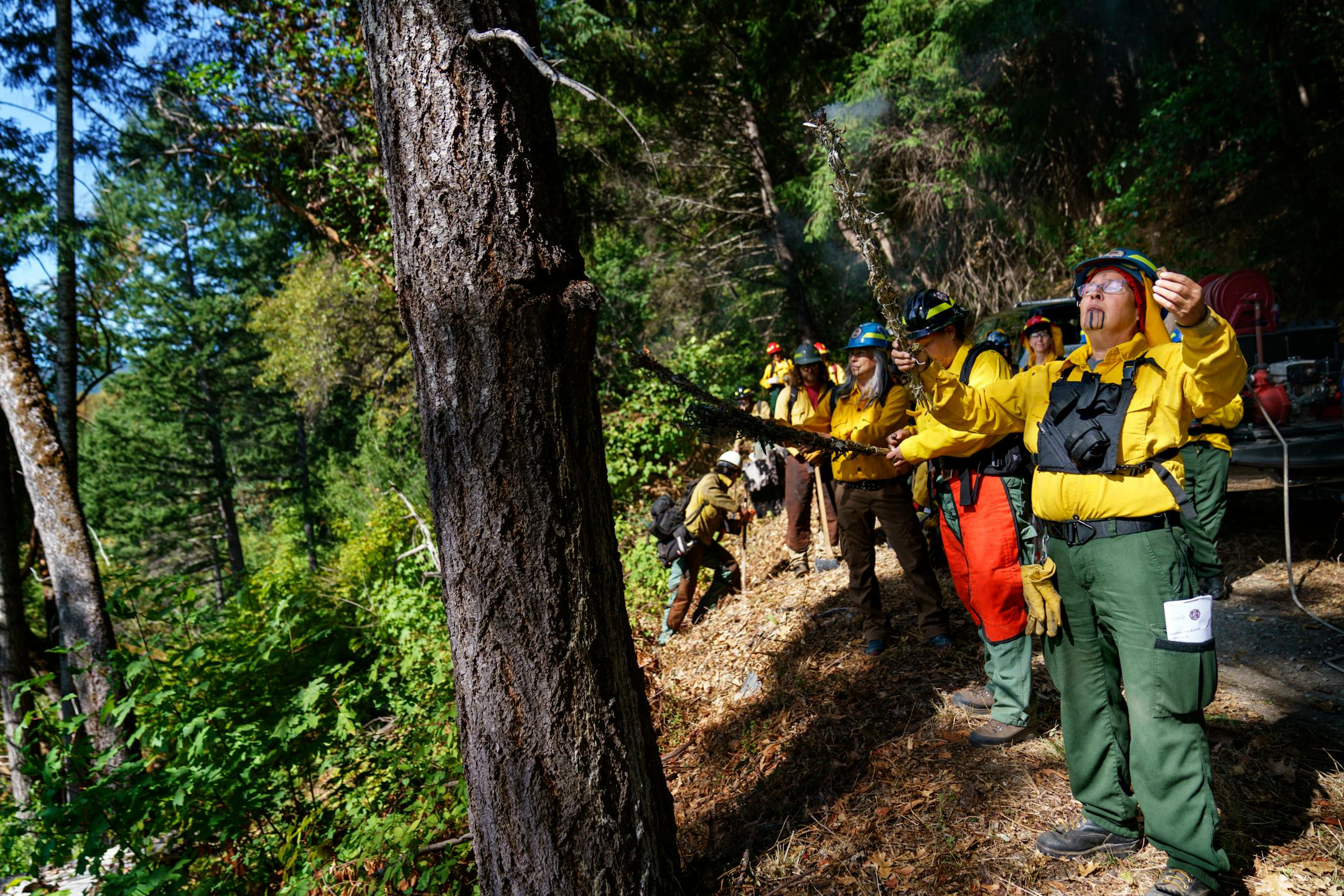 Elizabeth Azzuz stands in prayer with a handmade torch of dried wormwood branches before leading a cultural training burn on the Yurok reservation in Weitchpec, Calif., Thursday, Oct. 7, 2021. Azzuz, who is Yurok, along with other native tribes in the U.S. West are making progress toward restoring their ancient practice of treating lands with fire, an act that could have meant jail a century ago. But state and federal agencies that long banned "cultural burns" are coming to terms with them and even collaborating as the wildfire crisis worsens. (AP Photo/David Goldman) ORG XMIT: CADG201