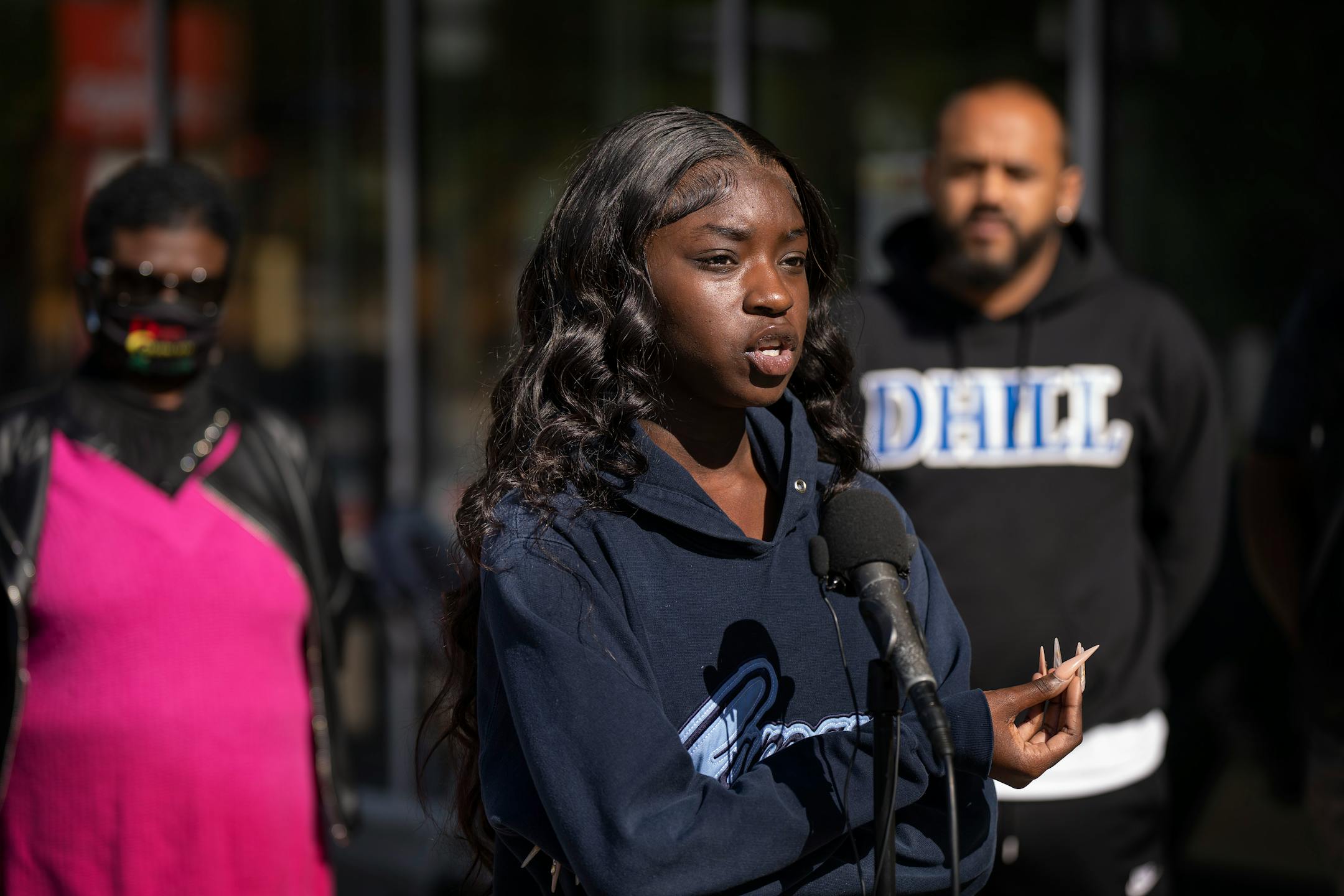 Black teenager in a sweatshirt stands in front of a microphone