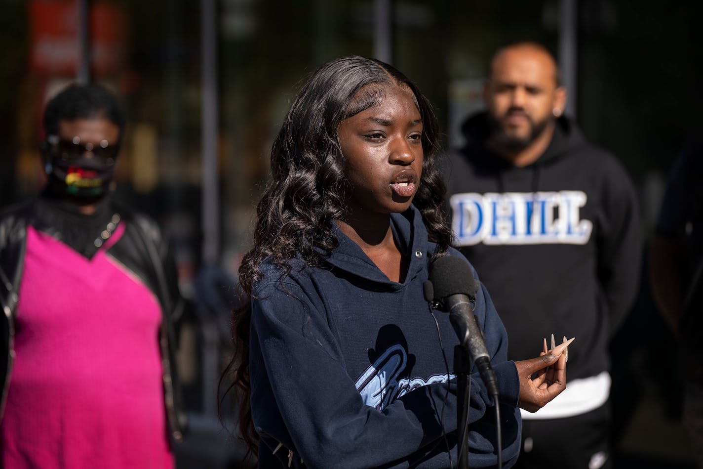 Black teenager in a sweatshirt stands in front of a microphone