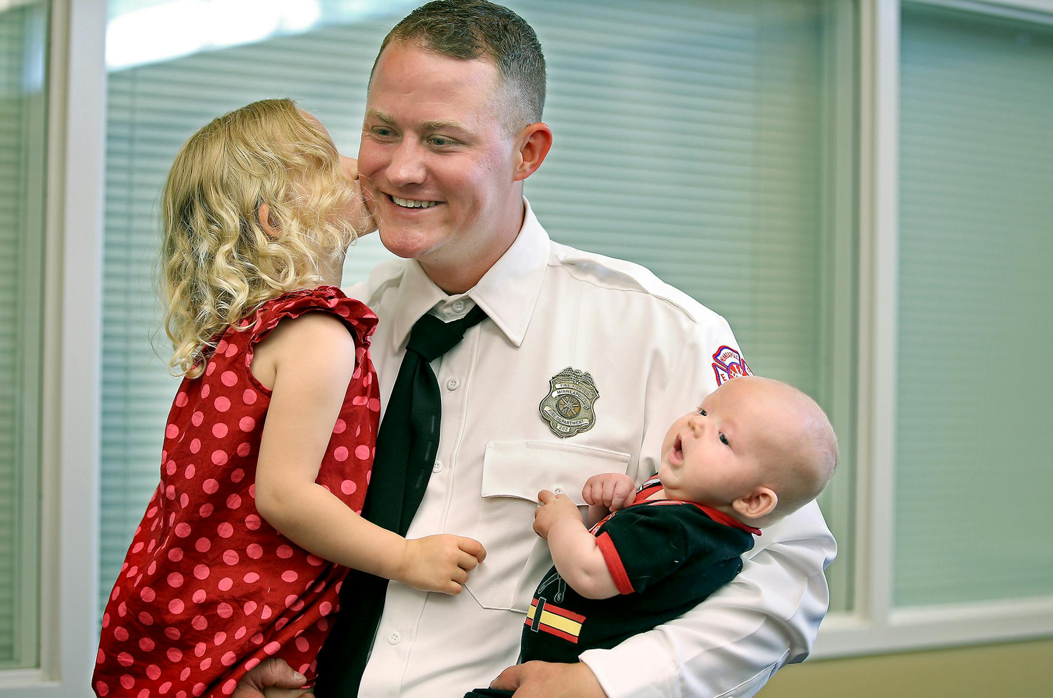 Newly inducted firefighter Jeffrey Rosener was given a kiss by his daughter Nina, 2, as he held his two-month-old son Calvin after their graduation ceremony at the Emergency Operations Training Facility, Friday, July 11, 2014 in Minneapolis, MN. Rosener served in the Marine Corps. ] (ELIZABETH FLORES/STAR TRIBUNE) ELIZABETH FLORES • eflores@startribune.com