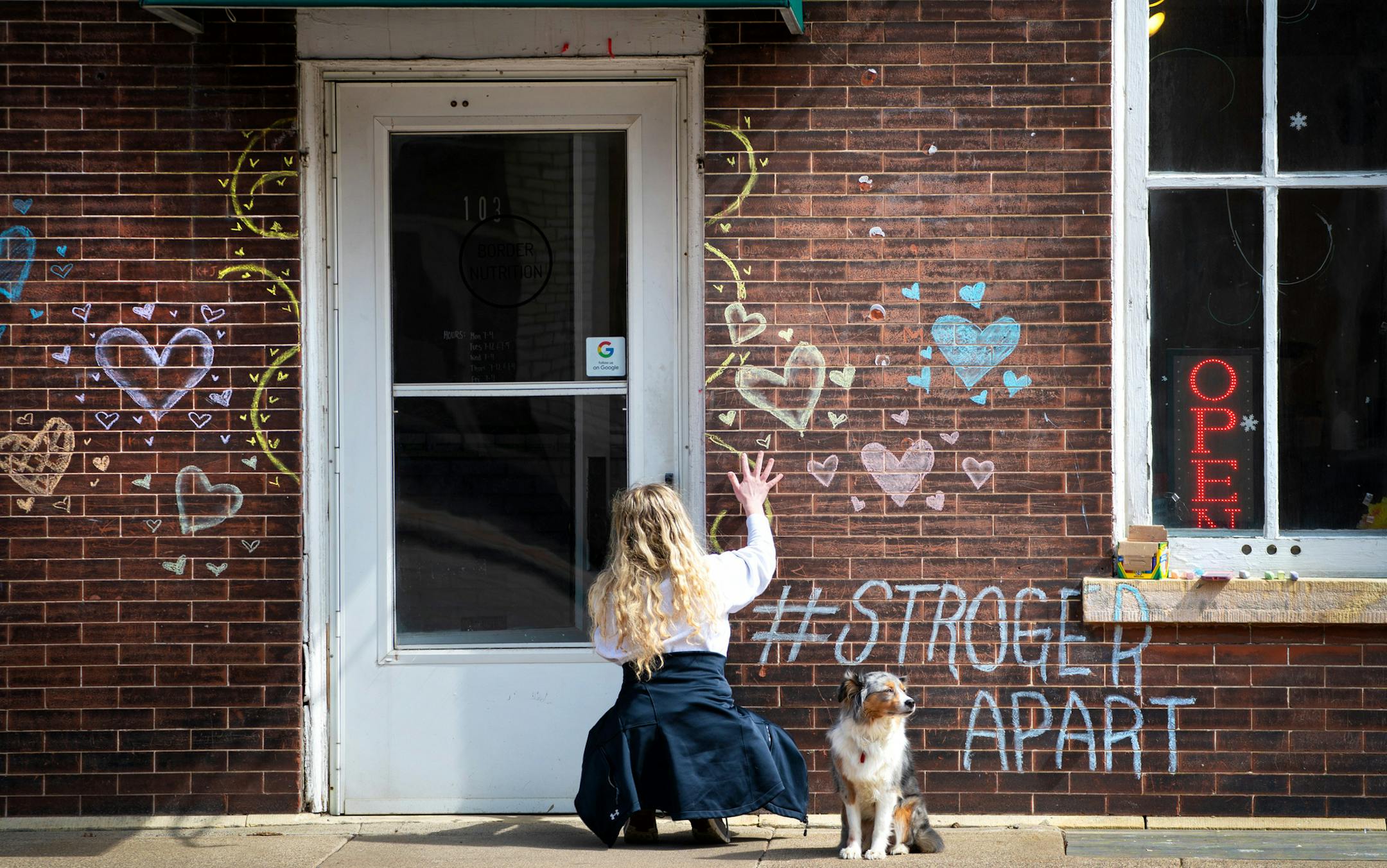 Ella looked up and down Sibley Street in Hastings on a warm sunny afternoon as her owner Whitney Owen drew chalk hearts, decorations and the hashtag #StrongerApart on her business Border Nutrition in Hastings, Minn.