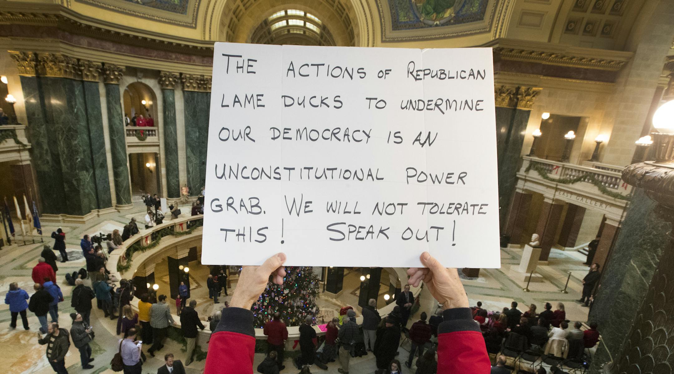 People protest the legislature's extraordinary session during the official Christmas tree lighting ceremony at the Capitol in Madison, Wis., Tuesday, Dec. 4, 2018. Demonstrators booed outgoing Wisconsin Gov. Scott Walker on Tuesday during the Christmas tree-lighting ceremony, at times drowning out a high school choir with their own songs in protest of a Republican effort to gut the powers of his Democratic successor. (Mark Hoffman/Milwaukee Journal-Sentinel via AP)