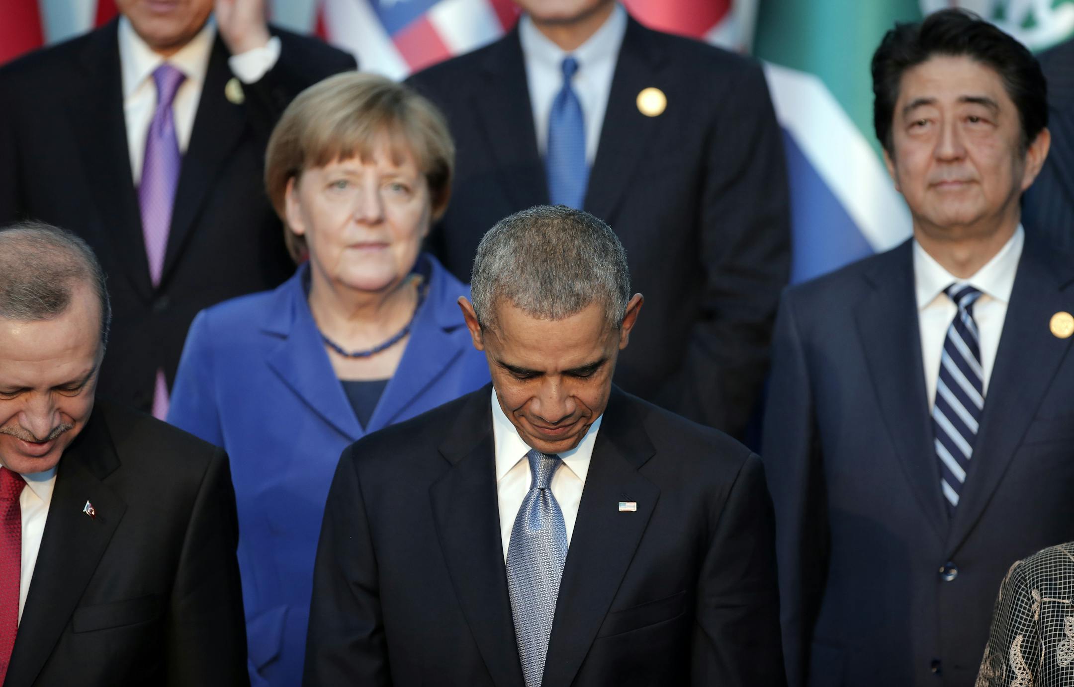 President Barack Obama, center, flanked by Turkish President Recep Tayyip Erdogan, left, looks down as German Chancellor Angela Merkel and Japanese Prime Minister Shinzo Abe, right, stand in background after posing for a family photo at the G-20 summit in Antalya, Turkey, Sunday, Nov. 15, 2015. U.S. President Barack Obama pledged Sunday to redouble U.S. efforts to eliminate the Islamic State group and end the Syrian civil war that has fueled its rise, denouncing the extremist group's horrifying