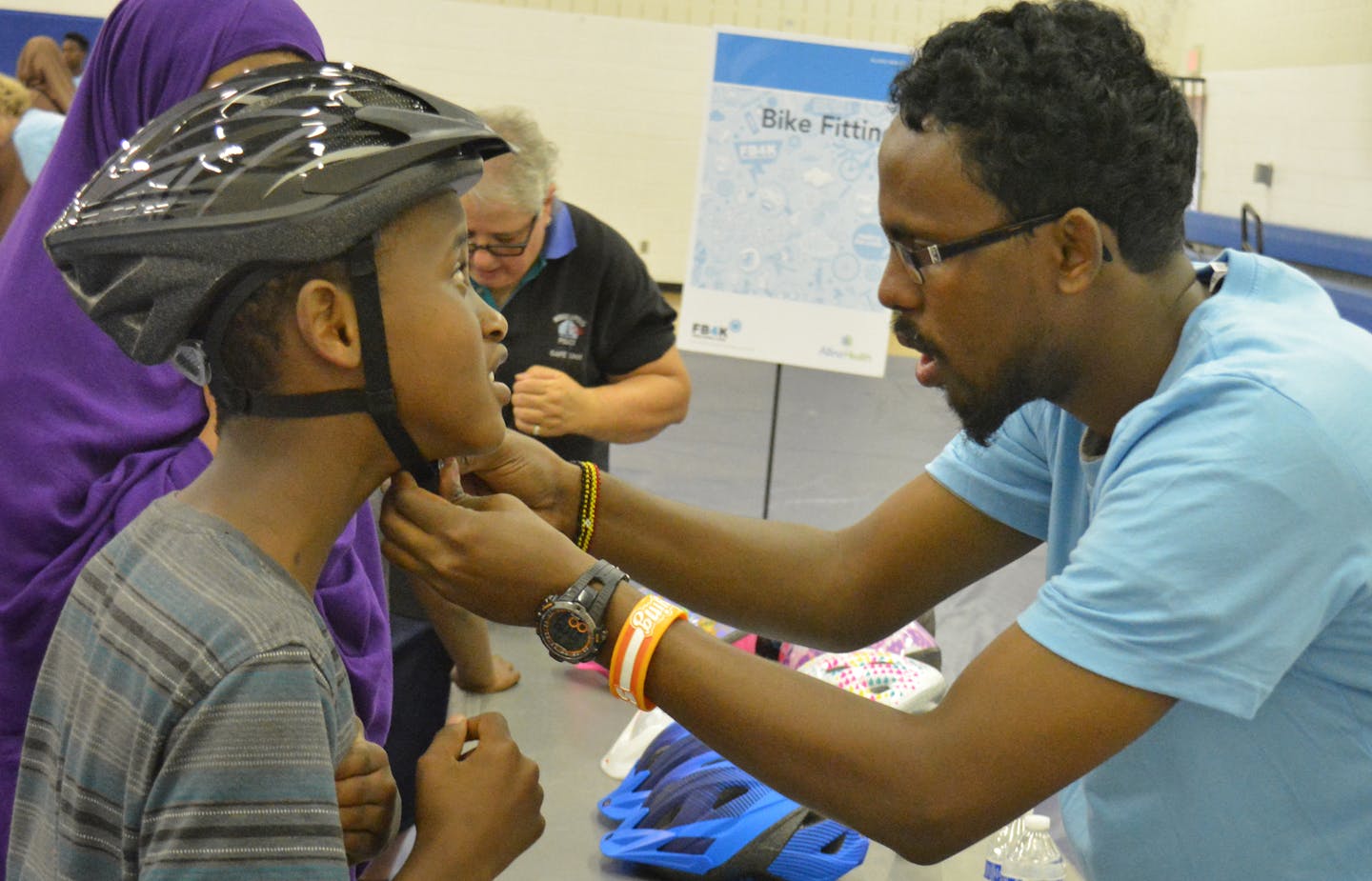 Assad Isak a volunteer helping a kid how to wear helmet in Brian Coyle Community Center. photo credit: Salman Yousafzai/ Star Tribune