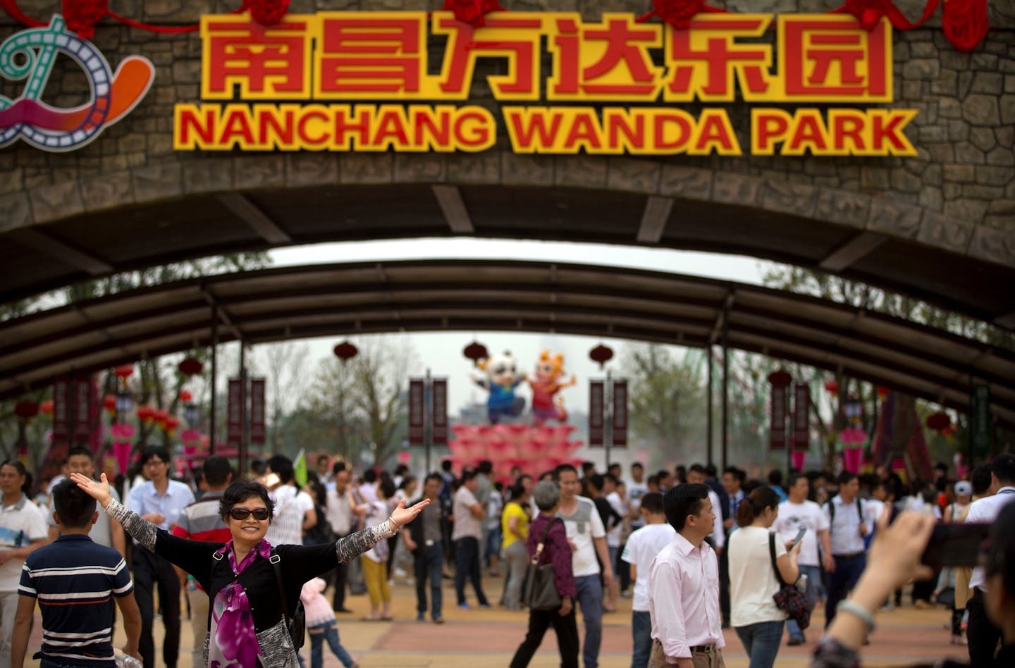 In this May 28, 2016, photo, a woman poses for a photo at the entrance gate during the grand opening of the Nanchang Wanda Park theme park in Nanchang in southeastern China's Jiangxi province. Chinese conglomerate Wanda Group, owner of Hollywood's Legendary Studios, is selling most of its theme parks, retreating from a business it once said would challenge Walt Disney Co. (AP Photo/Mark Schiefelbein) ORG XMIT: XMAS102