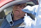 Carlos Garcia leans back as a medical professional inserts a swab into his nose to collect a sample to test for COVID-19 at a drive-through testing si