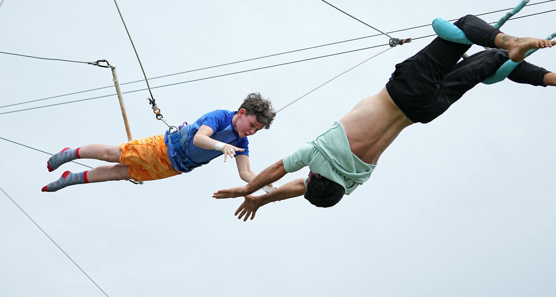 Everett Smith reaches for coach Matt Flynn while practicing a flying trapeze planche trick.