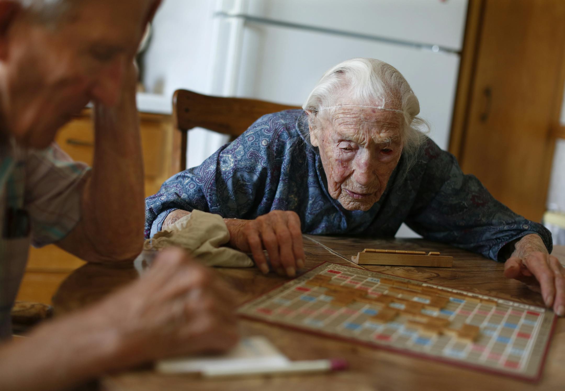 At her home in Pottsdam, Anna Stoehr plays Scrabble with her son Harlan,83 who is changing the hoses on her washer. She is perhaps the oldest person who lives alone. She does not have a special diet but likes to bakes her own bread. She also likes to eat liverwurst, butter, and bacon.