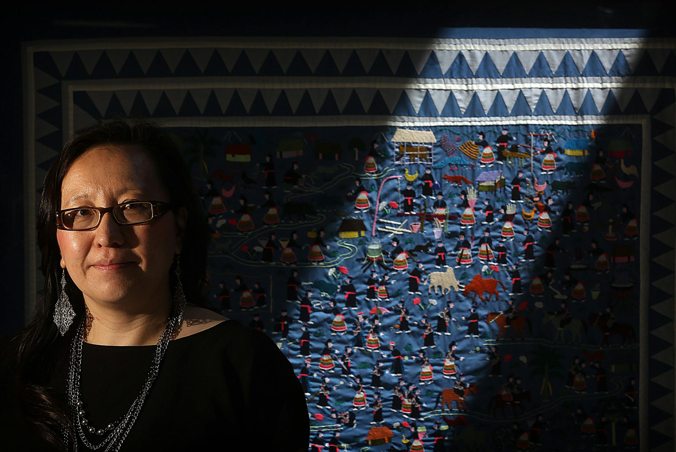 Be Vang of Phalen Lake Hmong Studies Magnet School, stands behind a Hmong story cloth. Vang will be principal at Mississippi Creative Arts in the fall.