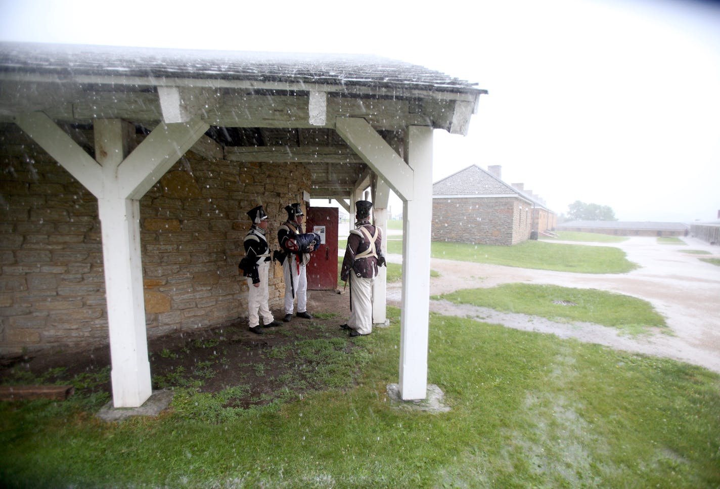 War re-enactors, Daryl Jorgenson, Tom Lalim and Michael Campbell wait under an overhang with the American flag for the drum roll to signal the raising of the flag at Fort Snelling.