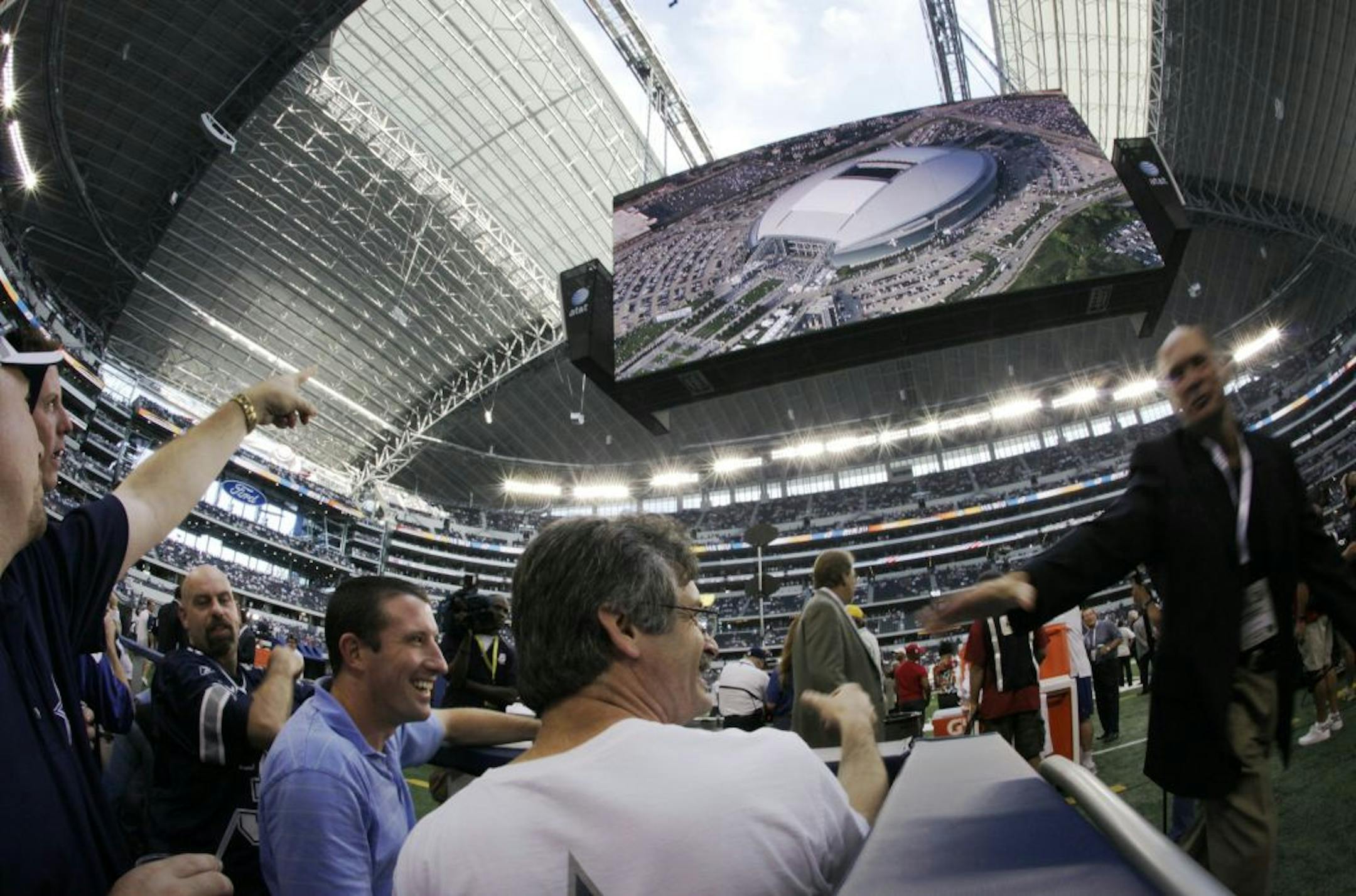 Football fans in the ground level suites, left, look on as the roof of Cowboys Stadium is opened as a live projection of the event is shown on the large video screen hanging over the field, before an NFL football game between the Dallas Cowboys and the New York Giants, Sunday, Sept. 20, 2009, in Arlington, Texas.