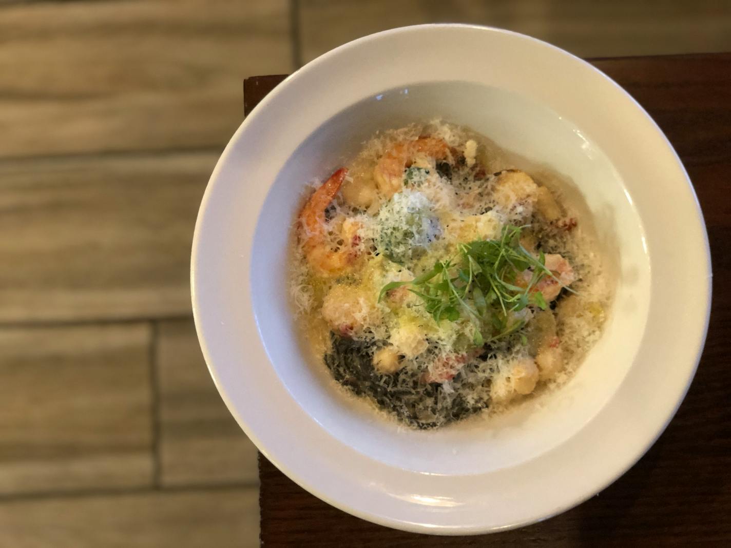 A bowl of squid ink pasta with baby spinach, Brussels sprouts, shrimp and scallops in a cream sauce.