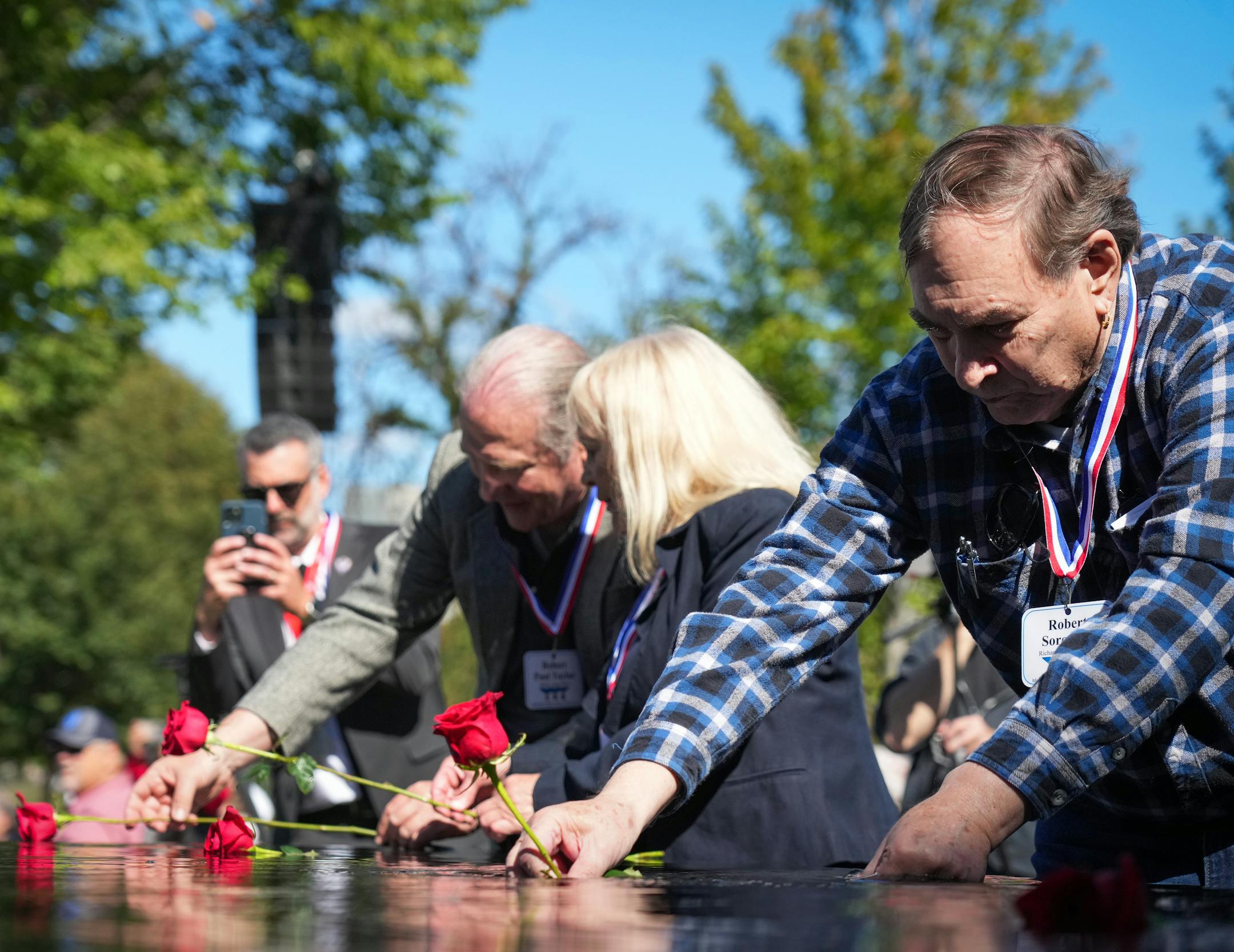 A handful of memorial attendees place long stem roses on the Minnesota Medal of Honor Memorial.