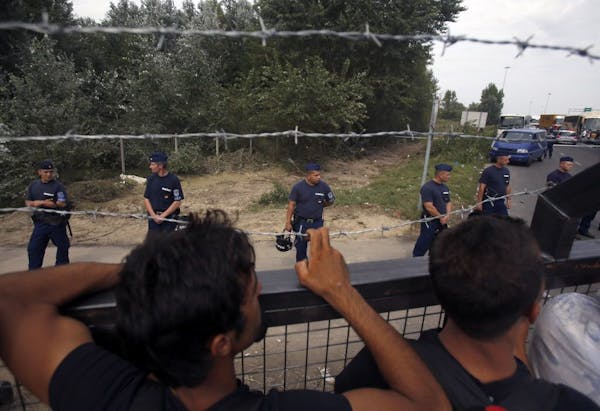 Migrants look over the fence as police officers stand guard at the Horgos border crossing into Hungary, near Horgos, Serbia, Tuesday, Sept. 15, 2015. 