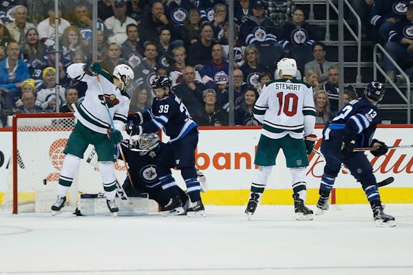 Minnesota Wild's Marcus Foligno, left, deflects the shot from the point past Winnipeg Jets goaltender Connor Hellebuyck (37) as Toby Enstrom (39) defe