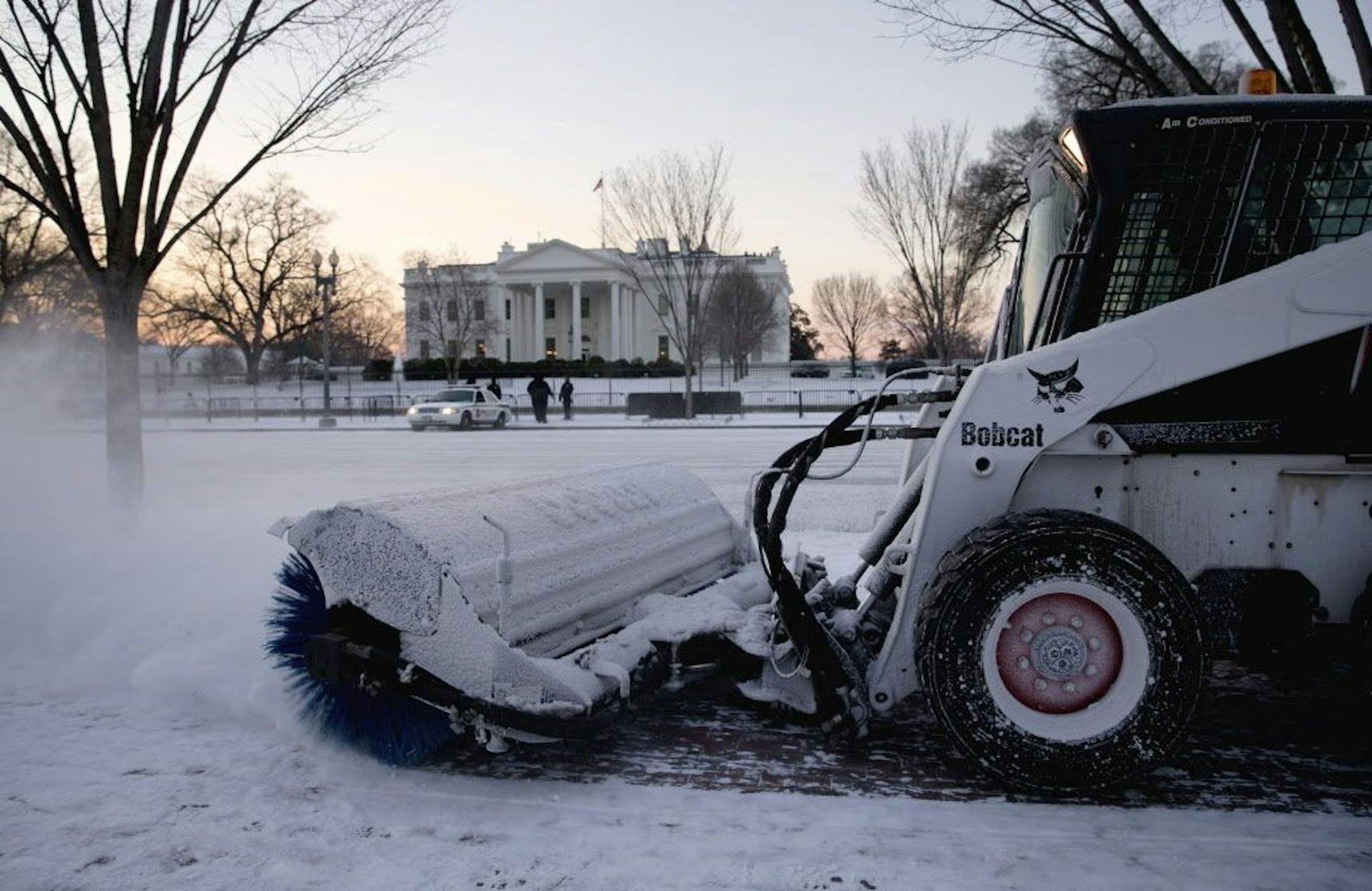A worker with the National Park Service sweeps snow along Pennsylvania Avenue in front of the White House in Washington, Thursday, Jan. 21, 2016, after an overnight dusting of snow hit the Washington area.