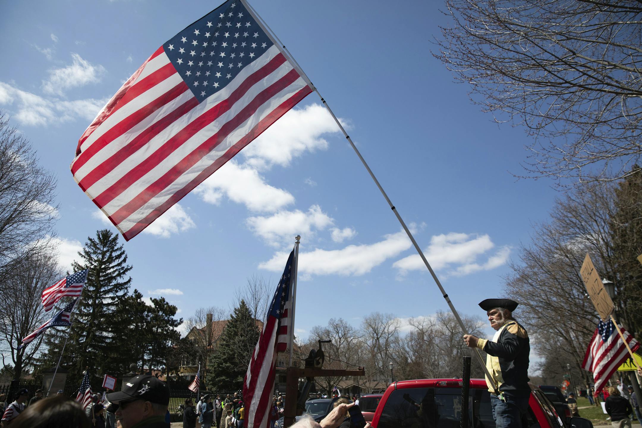 A man dressed in colonial style clothing waves a flag in the air and blows an airhorn from the back of a truck during a "Liberate Minnesota" protest in St. Paul, Minn., on Friday, April 17, 2020. A growing number of protests are being staged across the U.S. to oppose stay-at-home orders amid the coronavirus pandemic. (Evan Frost/Minnesota Public Radio via AP)