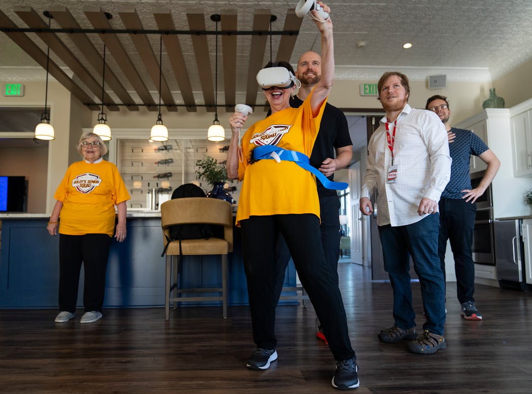 Brenda Hoffman triumphantly lands a punch in virtual-reality boxing as fellow resident Carole Johnson and (from left) personal trainer Ian Williams, occupational therapist Stanton Swanson and VR experience designer Dan Bodunov, all of FitVive, look on.