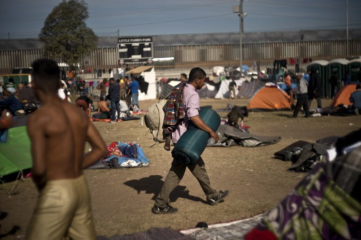 A man, part of the migrant caravan walks at a shelter in Tijuana, Mexico, Wednesday, Nov. 21, 2018, with the U.S. border in the background. Migrants camped in Tijuana after traveling in a caravan to reach the U.S are weighing their options after a U.S. court blocked President Donald Trump's asylum ban for illegal border crossers.