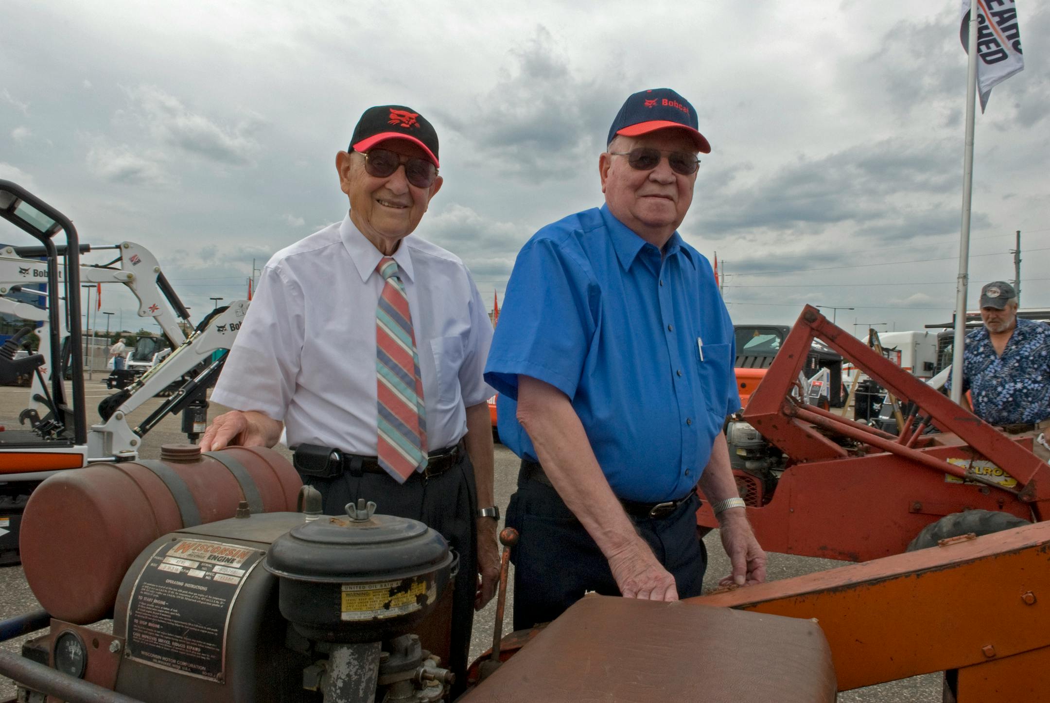 Bobcat creators Cyril Keller, left, and brother Louis with the seventh of seven original Keller Loaders, built in 1957. The Kellers demonstrated their first loader at the Minnesota State Fair in 1958. Behind them are new models that have come from their original design.