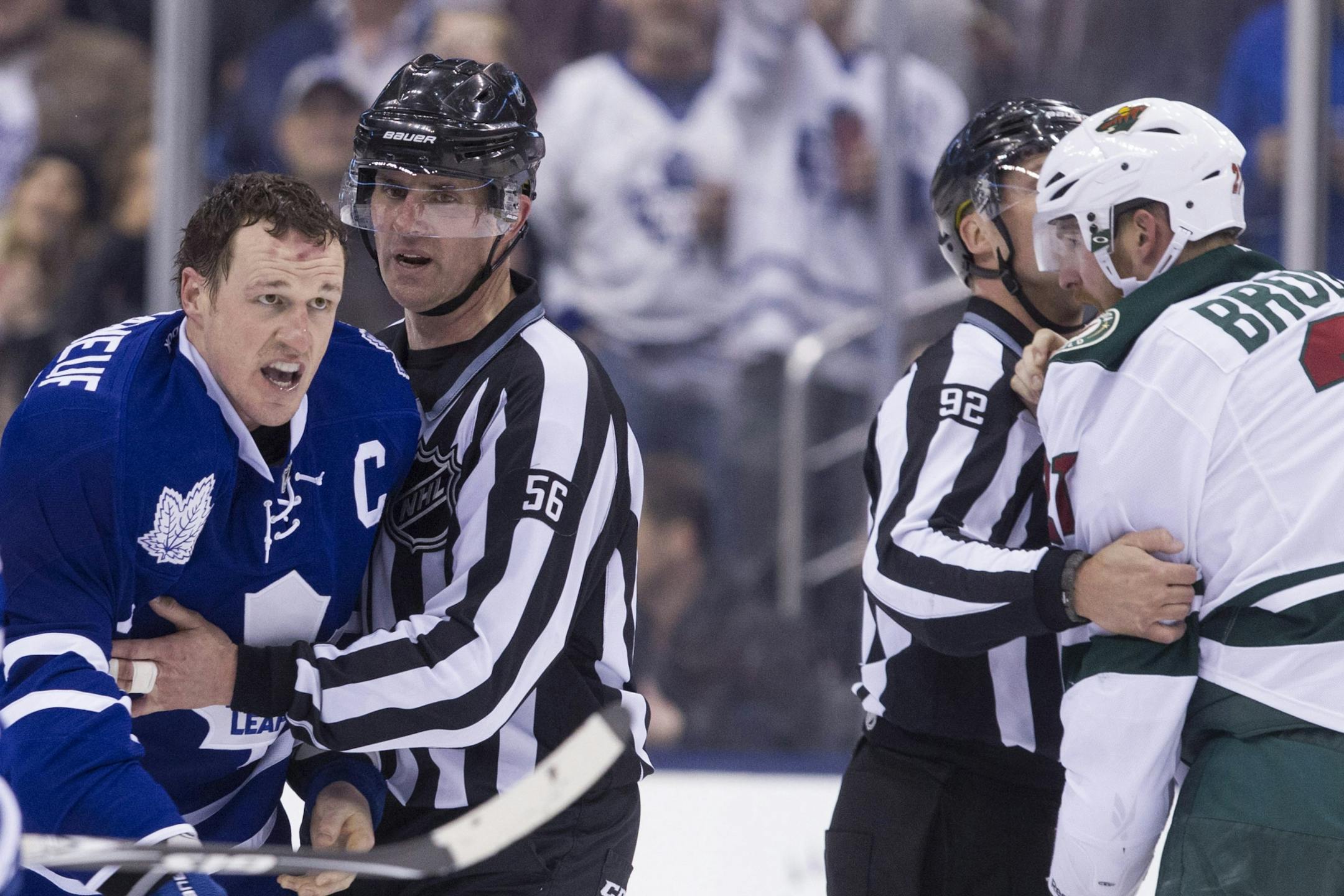 Referees separate Toronto Maple Leafs Dion Phaneuf, left, and Minnesota Wild's Kyle Brodziak, right, after fighting during second period NHL hockey action in Toronto on Monday, March 23, 2015.