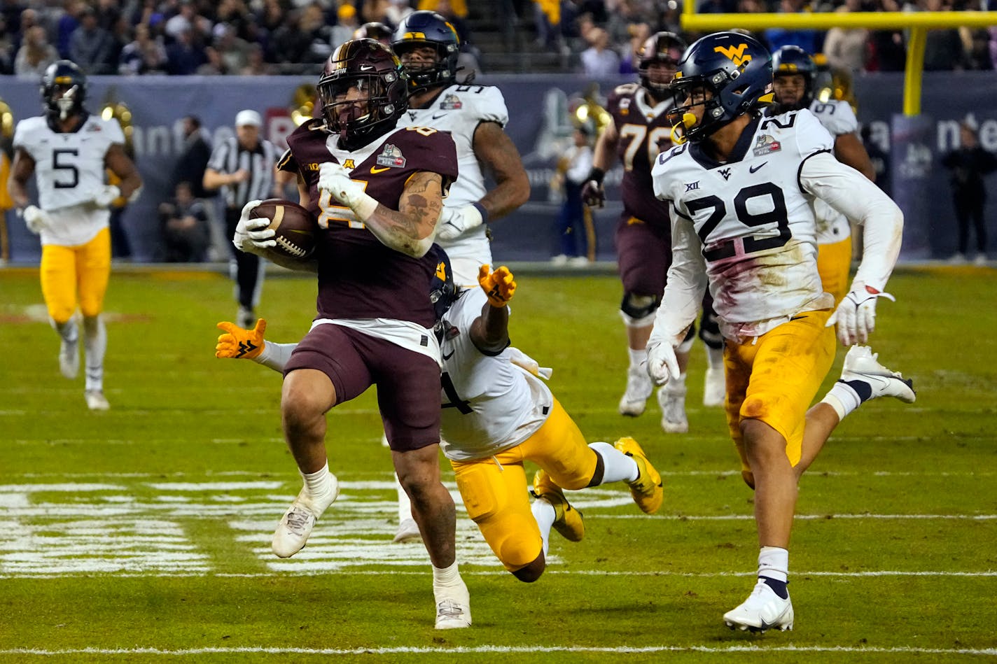 Minnesota running back Ky Thomas (8) runs away from West Virginia safety Alonzo Addae and safety Sean Mahone (29) during the first half of the Guaranteed Rate Bowl NCAA college football game Tuesday, Dec. 28, 2021, in Phoenix. (AP Photo/Rick Scuteri)