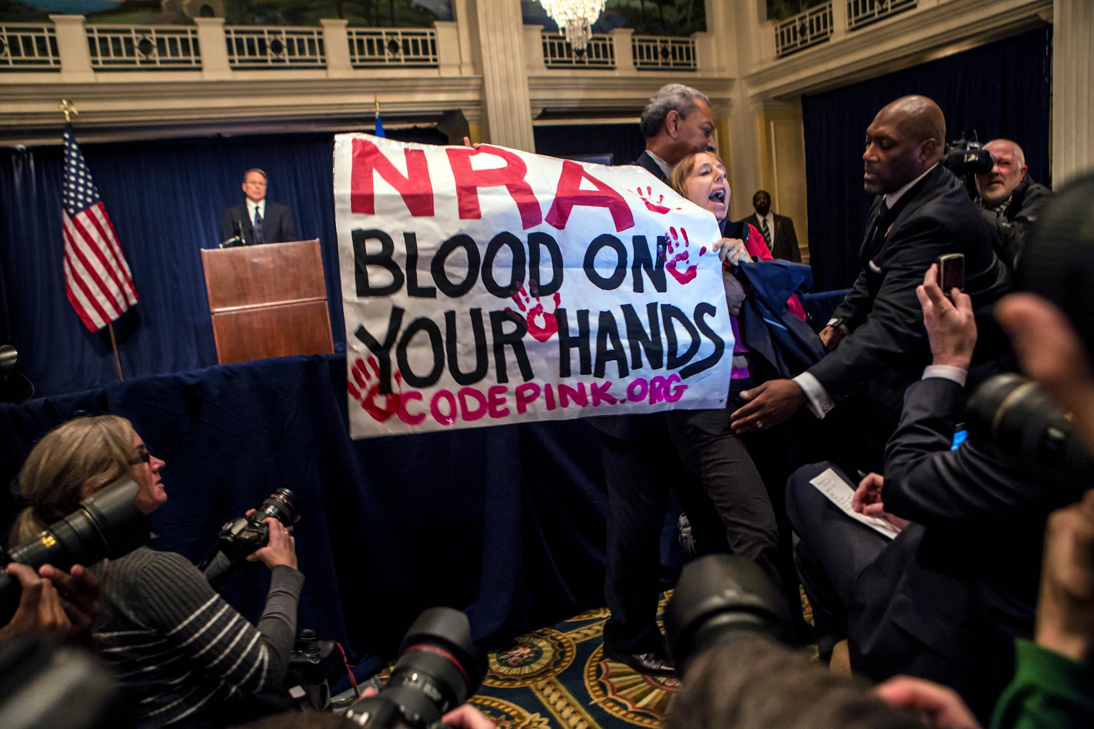 Medea Benjamin, co-founder of the group Code Pink, is removed from the room by security for interrupting a speech by Wayne LaPierre, the executive vice president of the National Rifle Association, in Washington, Dec. 21, 2012. During the news conference Friday, the NRA called for armed protection for each school in the country as the best way to protect children from gun violence.