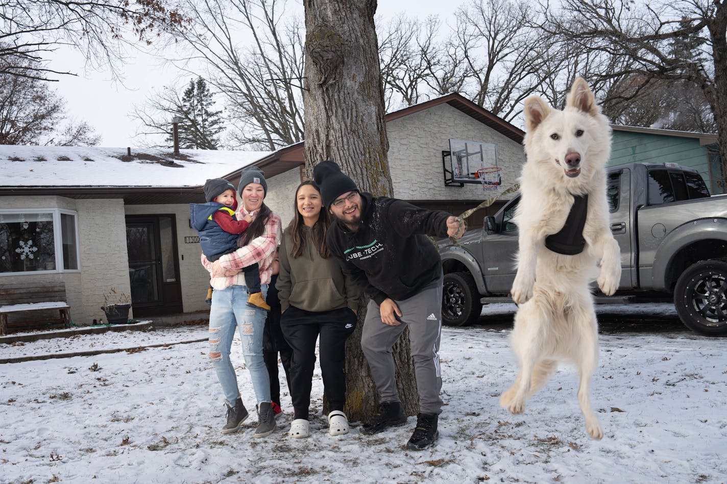 Kellie Basswood, her partner William Lussier and their children William Jr., 2, Chance, 7, (hiding behind them) and Jade 12, along with the family's leaping 9-month-old puppy Goon, which is Ojibwe for snow, outside their home Friday, Jan. 12, 2024 Champllin, Minn. First time homebuyer Kellie Basswood and her partner William Lussier were able to purchase this home with the help of the Mni Sota Fund, a wealth building nonprofit that works with Native families to help bridge the homeownership gap between white and Native Minnesotans. ] GLEN STUBBE • glen.stubbe@startribune.com