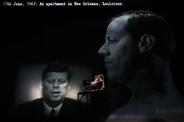 Images of President John F. Kennedy and assassin Lee Harvey Oswald are projected onstage as Oswald (played by Michael Milligan, center) watches Kenned