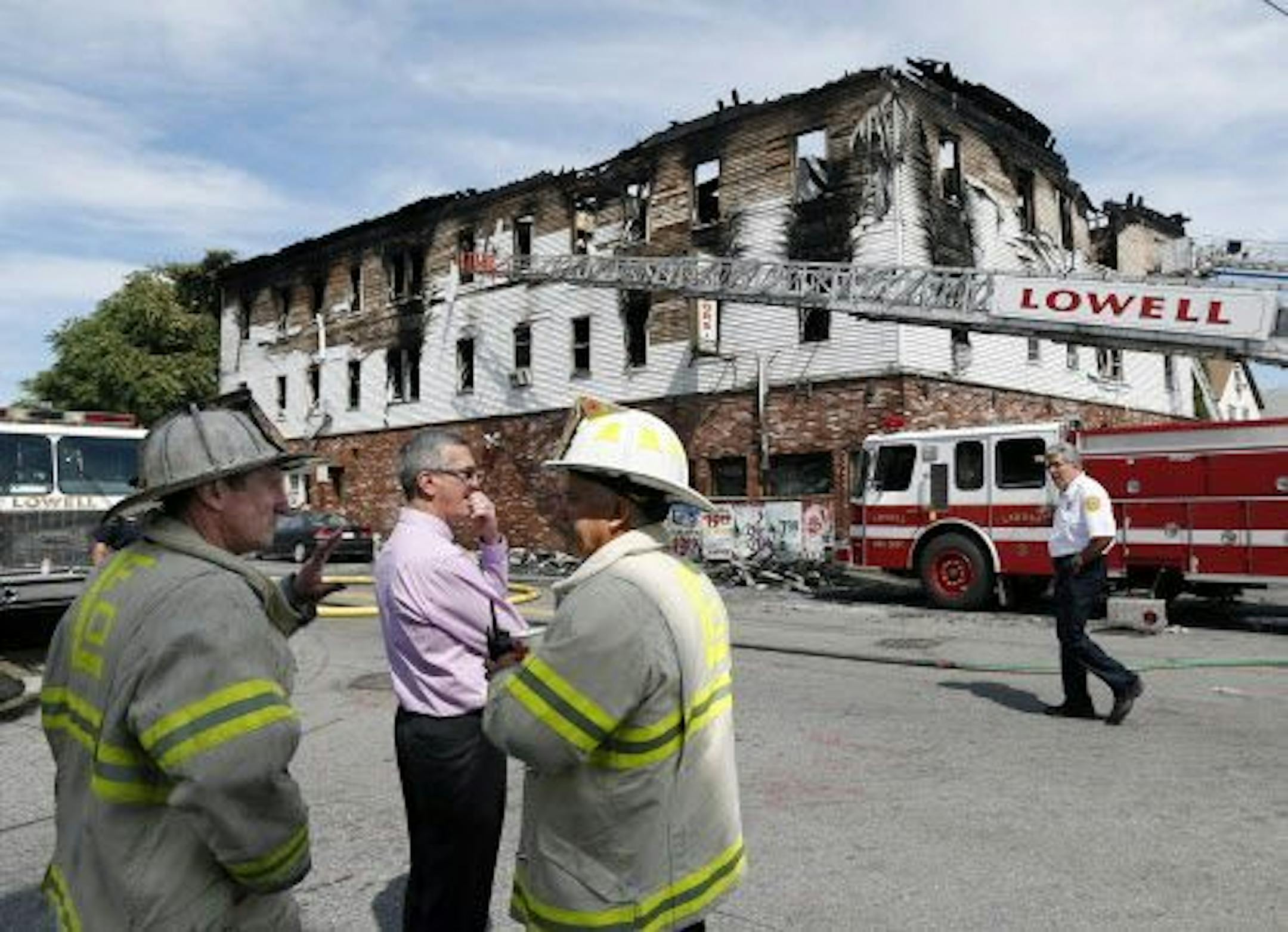 Fire officials observe the scene of a burned three-story apartment and business building in Lowell, Mass., Thursday, July 10, 2014.