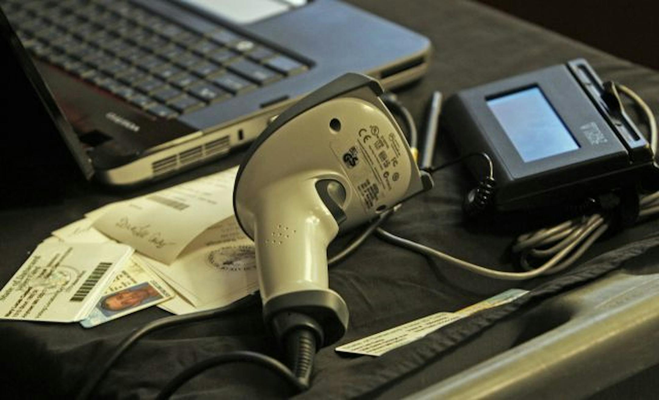 A voter ID scanning device made by Datacard Group. The system includes a scanner, left, digital signiture pad with stylus and a computer to input voter information.