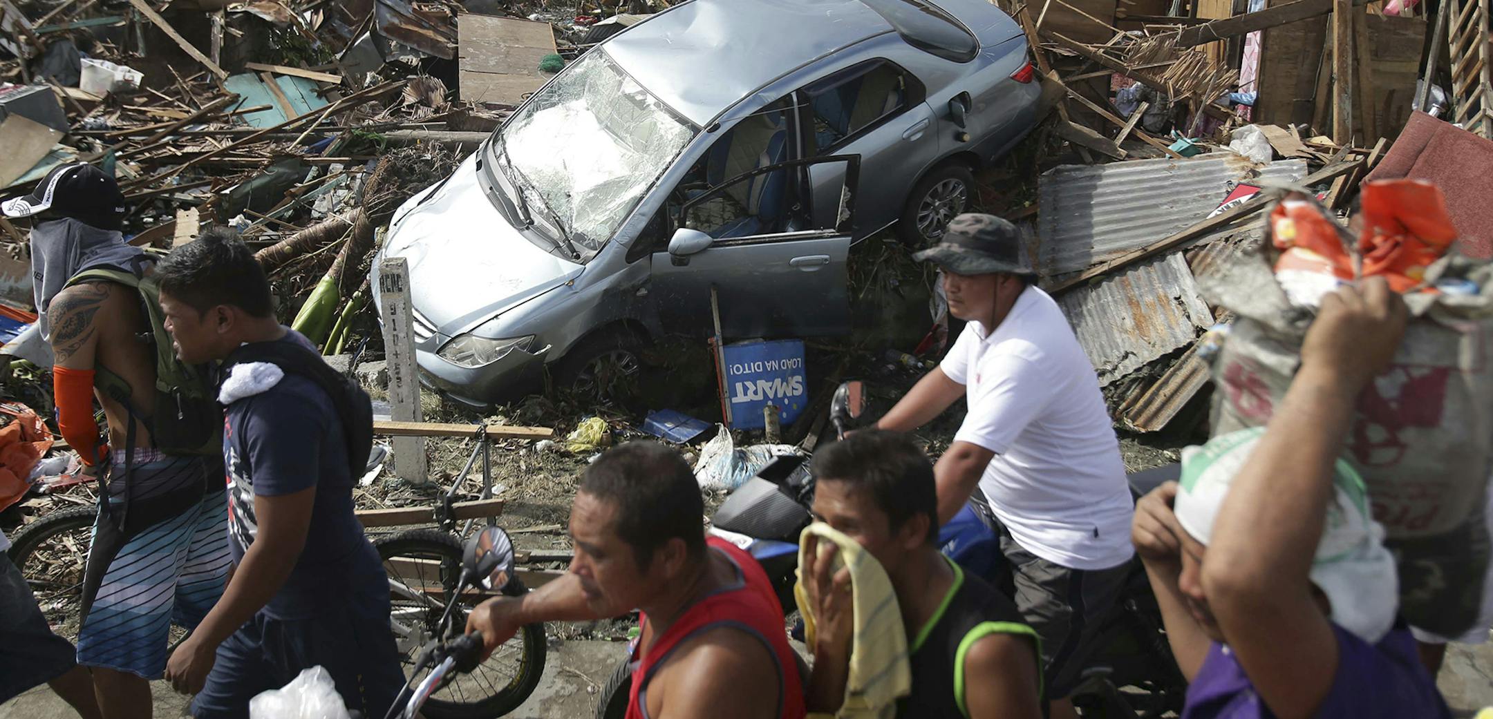 Survivors move past the damage caused by Typhoon Haiyan in Tacloban city, Leyte province, central Philippines on Monday, Nov. 11, 2013. The typhoon-ravaged Philippine islands faced an unimaginably huge relief effort that had barely begun Monday, as bloated bodies lay uncollected and uncounted in the streets and survivors pleaded for food, water and medicine. (AP Photo/Aaron Favila) ORG XMIT: MIN2013111113101042