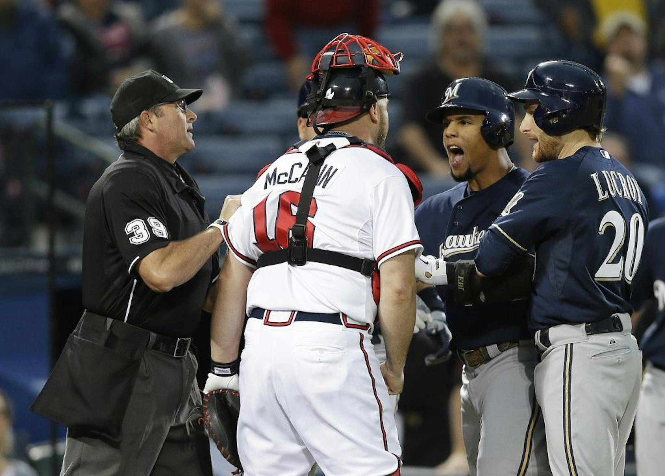 Milwaukee Brewers' Carlos Gomez (27) and Atlanta Braves catcher Brian McCann (16) are separated by home plate umpire Paul Nauert and Brewers' Jonathan Lucroy (20) as they exchange words following a home run by Gomez in the first inning of a baseball game Wednesday, Sept. 25, 2013 in Atlanta.