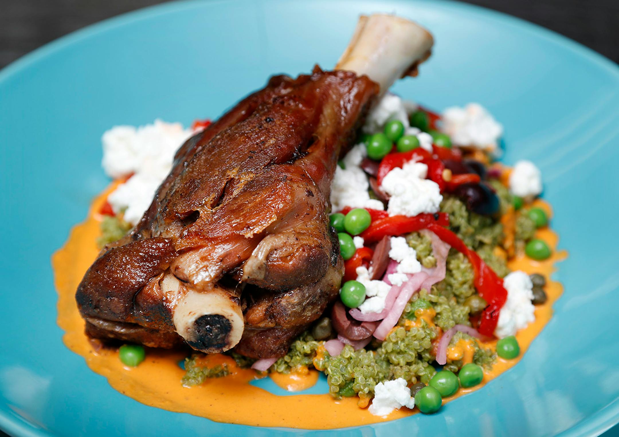 Lamb and Quinoa with Mint Pesto. Slow roasted lamb shank served on abed of quinoa tossed mint pesto. Topped with kalamata olives, capers, roasted red peppers, sweat peas, brined red onions and goat cheese.