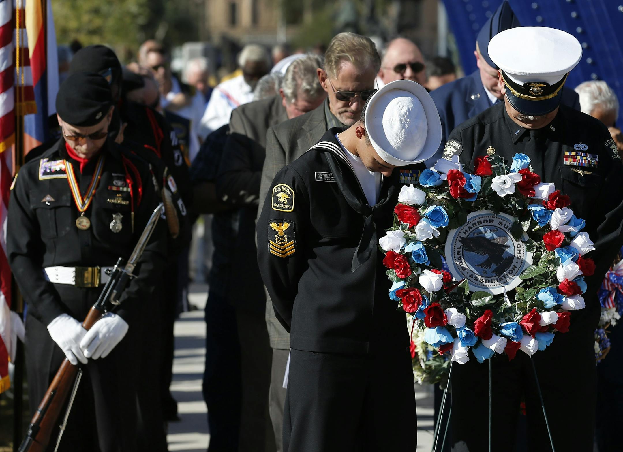Members of the Naval Sea Cadets, middle and right, and a member of the POW MIA KIA Honor Guard, left, bow their heads during a prayer at the Pearl Harbor Remembrance Day ceremonies in front of the USS Arizona Memorial Monday, Dec. 7, 2015, in Phoenix. (AP Photo/Ross D. Franklin)