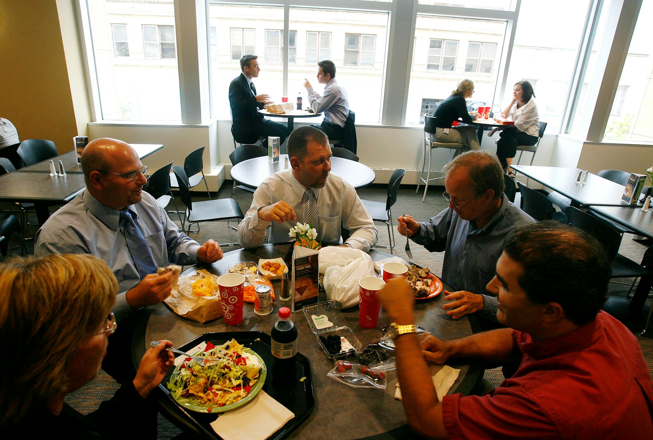 In a tight economy, more people are scaling back on lunches and bringing in their meals, including three of the five diners at this table at the Target corporate cafe in downtown Minneapolis. Ron Sherman, upper left, and Joe Schovronski, right to left and Bob Huser, brought their own lunches to Target with them Wednesday. Schovronski says he always brings a lunch and budgets himself a mere $5 a week for dining out. While Huser also brings his lunch his is not the typical brownbag fare. Wednesday