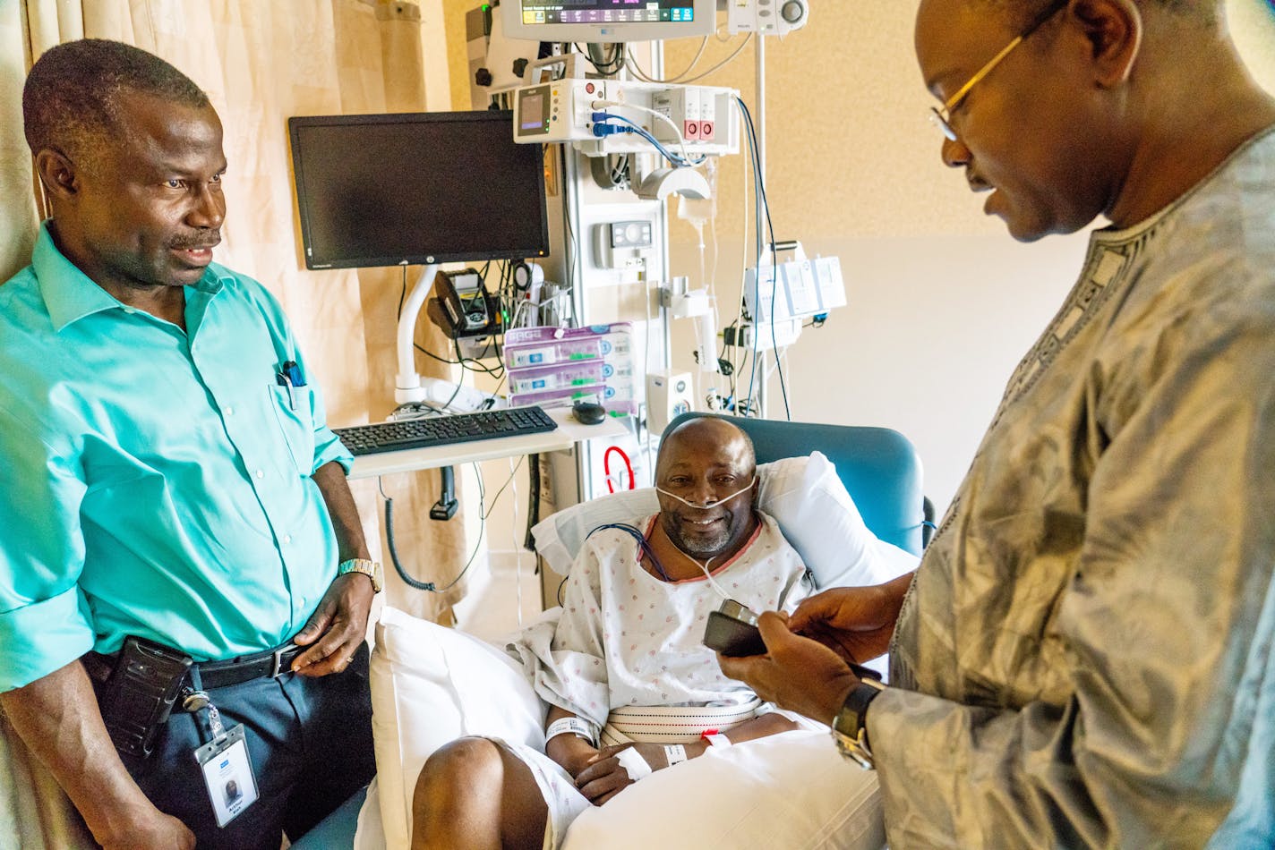 Mohammed Dukuly (center) listened to well wishers over a phone held by his uncle who shares the same name, Imam Mohammed Dukuly (right). ] MARK VANCLEAVE &#xa5; Mohammed Dukuly, a paraprofessional at Harrison Education Center, recovered at HCMC on Thursday, May 24, 2018. Corey David Burfield, 18, of St. Paul, was charged with one count of first-degree assault and one count of third-degree assault for the beating at the school.