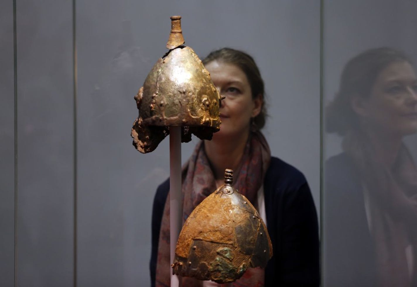 A British museum employee poses for the photographers behind a display of Viking helmets at a new exhibition entitled 'Vikings: Life and Legend' at the British Museum in central London, Tuesday, March 4, 2014.