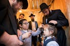 Shaya Feller, left, 9, with his father Rabbi Mendel Feller, top left, takes his turn cutting a lock of hair from Yosef Reindorp during his upsherin as
