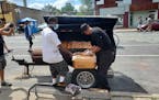 Dwight Alexander (right) places chicken wings into his smoker, on the street in front of his takeout restaurant Smoke in the Pit, steps from where Geo