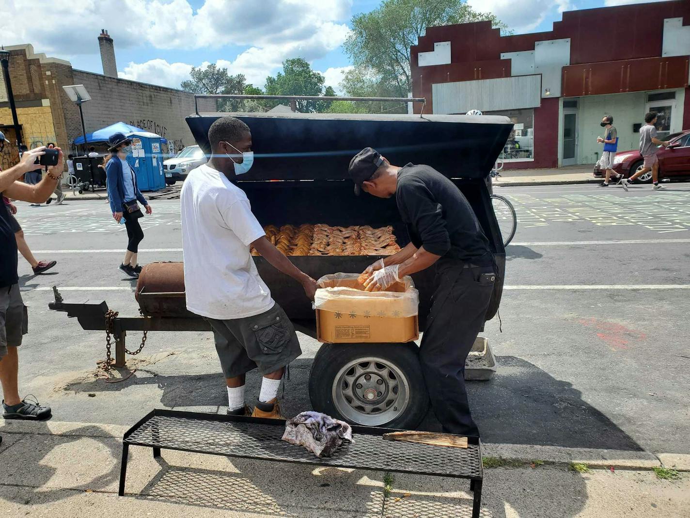 Dwight Alexander (right) places chicken wings into his smoker, on the street in front of his takeout restaurant Smoke in the Pit, steps from where George Floyd was killed by police. He gives away some of the wings to the people who visit the corner. "They forget about the sadness for five minutes when they eat this food," he said.